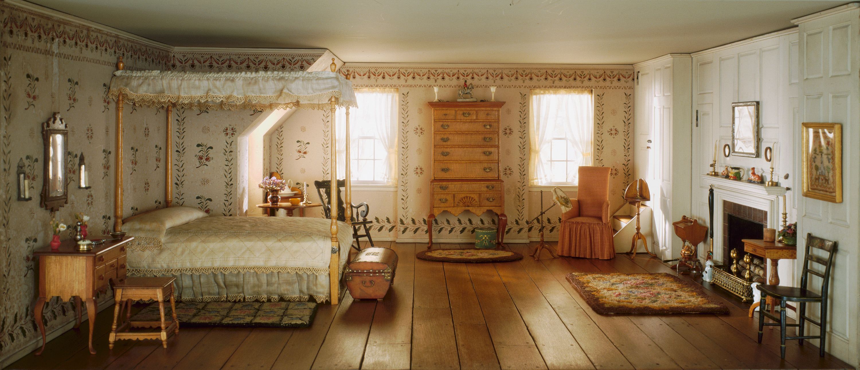 A miniature model of a New England type bedroom with wood floors and a four-poster bed.