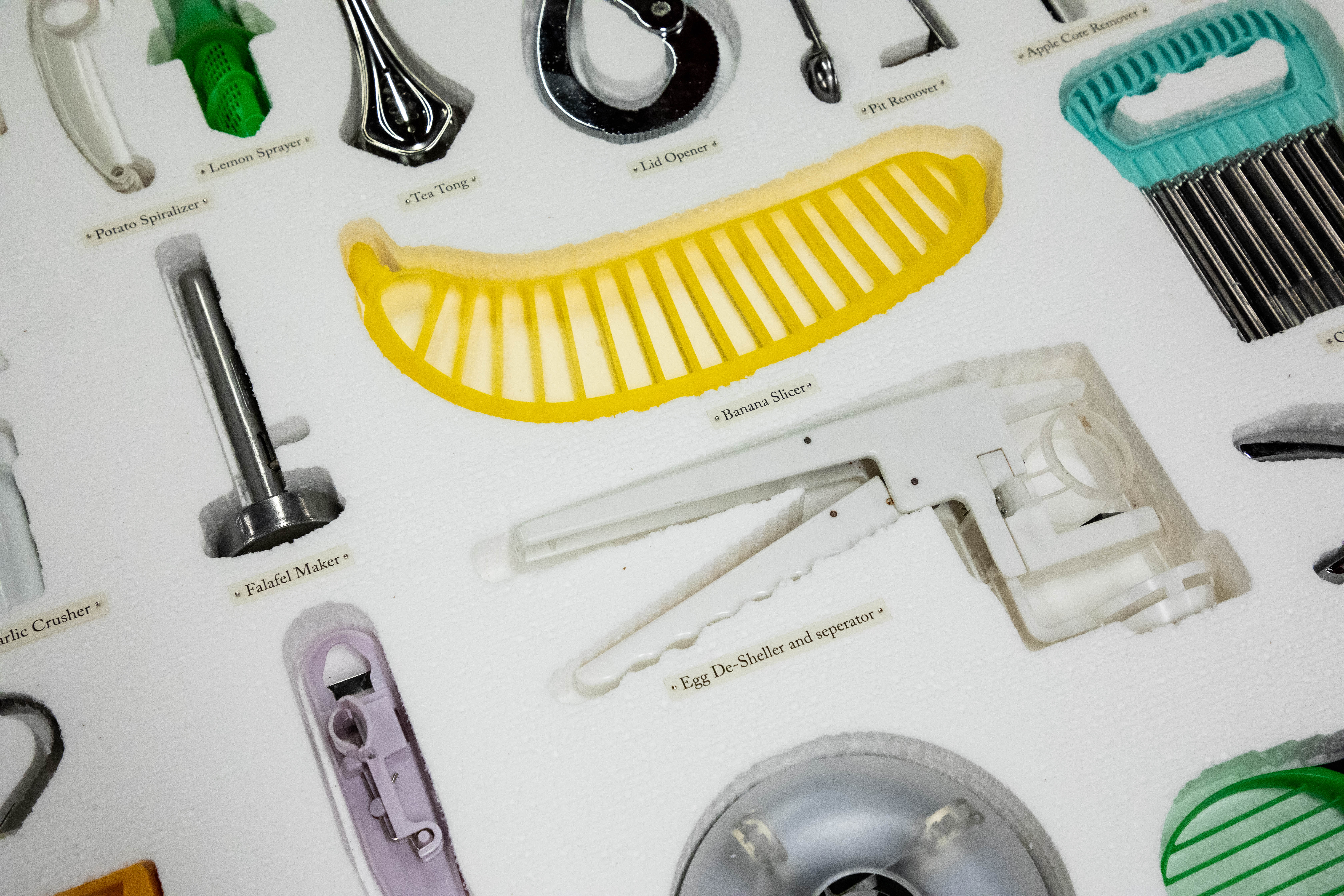 Close up photo of different types of kitchen utensils (banana slicer, falafel maker) resting in a sheet of styrofoam.